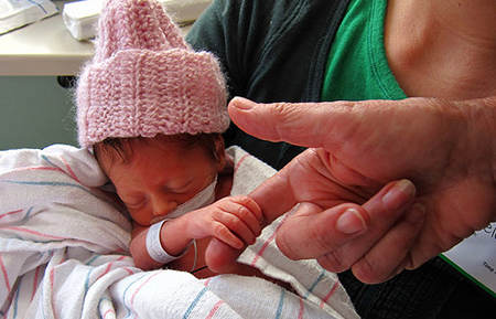 Infant in pink cap and feeding tube grabs a finger