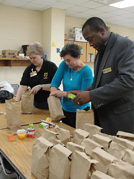 Coordinator Janet Cavin and volunteers from Balwin County organize food items into brown bags to provide 40 students with a small meal for the weekend.